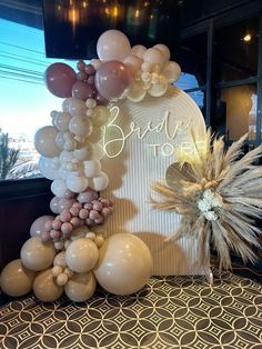 balloon arch with bride to be sign surrounded by balloons and flowers on the floor in front of a window