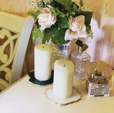 three white candles sitting on top of a table next to a vase filled with flowers