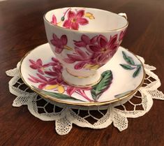 a tea cup and saucer with pink flowers on it sitting on a doily