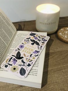 an open book sitting on top of a wooden table next to a candle and some books