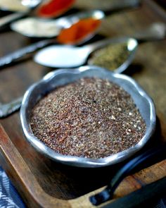 a metal bowl filled with spices sitting on top of a wooden table next to spoons