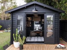 a small black shed sitting on top of a wooden deck next to a green plant