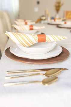 the table is set with plates, silverware and orange napkins on top of them