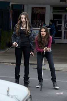 two girls on roller skates in the street with one holding a cane and another looking at something