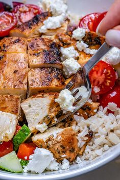 someone cutting into a salad with chicken, tomatoes and cucumbers