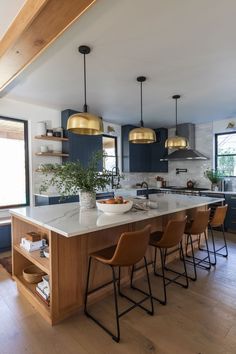 a kitchen with blue cabinets and gold pendant lights above the island countertop is surrounded by brown chairs