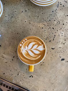 a cappuccino with leaves on it sitting on a counter next to plates