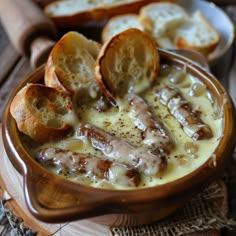 a bowl filled with cheese and bread on top of a wooden table next to slices of bread