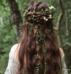 a woman with long brown hair and flowers in her hair is standing in the woods