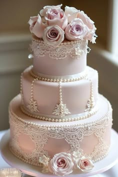 a three tiered wedding cake with pink roses on top and pearls around the edges