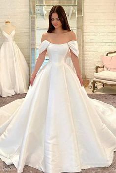 a woman standing in front of a mirror wearing a white wedding dress with off the shoulder sleeves