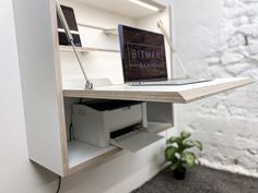 a desk with a laptop on top of it and a plant in the corner next to it