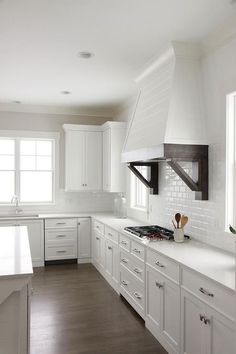 a kitchen with white cabinets and counter tops, an island in front of the stove