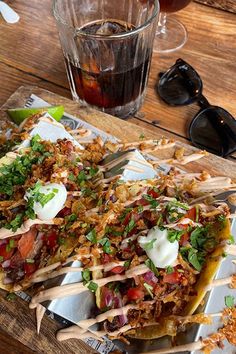 two tacos with toppings sit on a tray next to a glass of soda