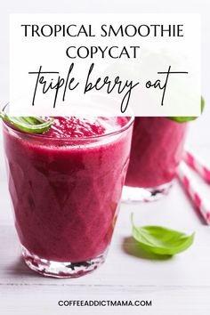 two glasses filled with tropical smoothie on top of a white table next to green leaves