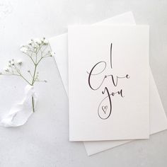 two cards with the words i love you written on them next to some white flowers