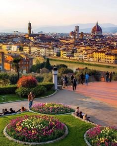 people are sitting on benches in the middle of a flower garden and looking at the city