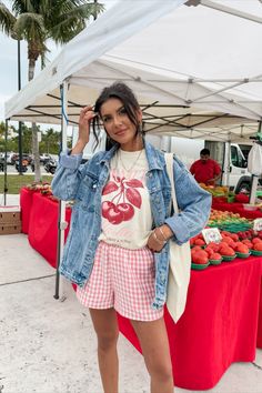 a woman standing in front of a table with fruit on it and wearing a jean jacket