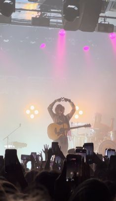 a man playing guitar in front of a large crowd at a concert with his hands up