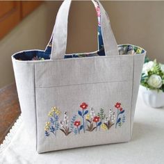 an embroidered bag sitting on top of a table next to a vase with flowers in it