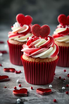 three red cupcakes with white frosting and hearts on top