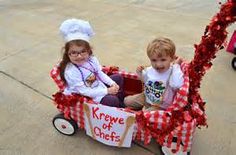 two young children are sitting in a wagon decorated with red and white decorations, one is holding a sign that says krewe of chefs