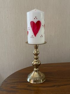 a white candle with a red heart painted on it sitting on a table next to a wall