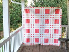 a red and white checkered quilt on a porch with a bench in the foreground