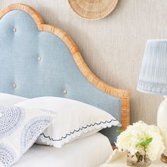 a blue headboard with white pillows and flowers on it next to a lamp in a bedroom