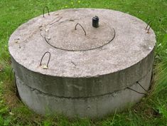 an old concrete circular object sitting in the middle of some grass with wires sticking out of it