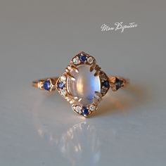 a ring with an oval stone surrounded by blue and white sapphires on a table