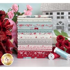 a stack of red and white fabric next to some pink flowers with one roll of thread