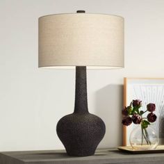 a table lamp sitting on top of a dresser next to a vase with flowers in it