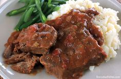 a white plate topped with meat and gravy on top of mashed potatoes