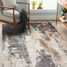 a living room area with a chair and rug on the hardwood floor, in front of a window