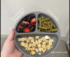 a person holding a plate with different foods in it that include berries, green beans and strawberries