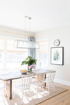 a dining room table with white chairs and a bowl of fruit on top of it