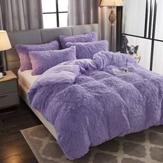 a bed covered in purple fluffy blankets and pillows