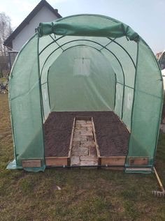 a green house that is in the grass with some dirt on it's ground