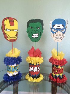 four paper masks are sitting on top of a glass table with red, yellow and blue pom - poms