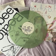 a green vinyl record sitting on top of a bed next to some posters and papers