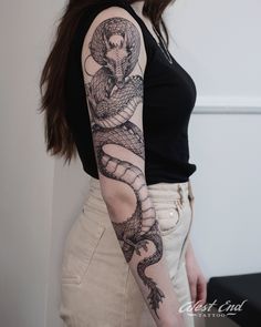 a woman with a snake tattoo on her arm and shoulder, standing in front of a white wall