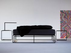 a bed sitting in front of a painting on a wall next to two black stands