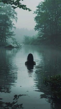 a person in the water with their back turned to the camera and trees behind them