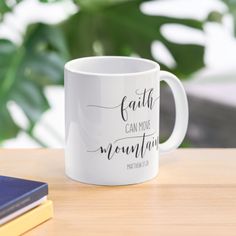 a white coffee mug with the words faith can move mountains on it next to some books