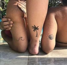 two women sitting next to each other with tattoos on their legs and one has a palm tree