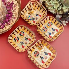 four decorative trays sitting on top of a red table next to a potted plant