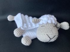 a crocheted sheep laying on top of a black floor next to a white blanket