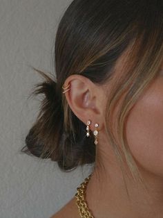 a close up of a woman's ear wearing gold earrings and a chain necklace