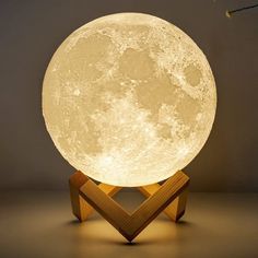 the moon lamp is on top of a wooden stand and it's turned on